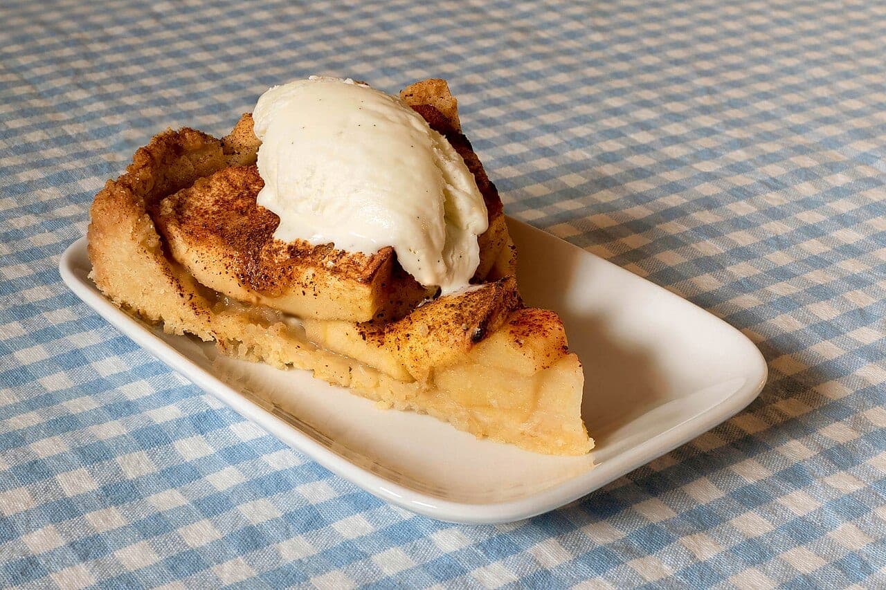 A slice of apple pie topped with a scoop of vanilla ice cream